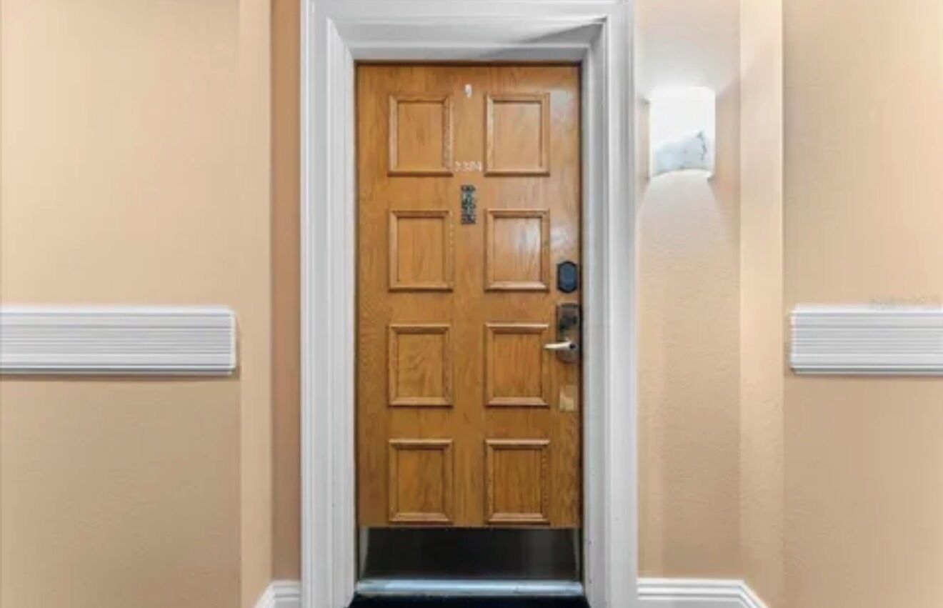 Une porte en bois avec une poignée en métal et une petite plaque, encadrée de moulures blanches.