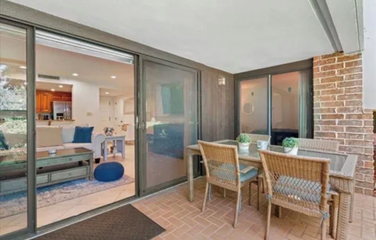 A modern interior with a dining area, a kitchen visible through glass doors, and a brick wall.
