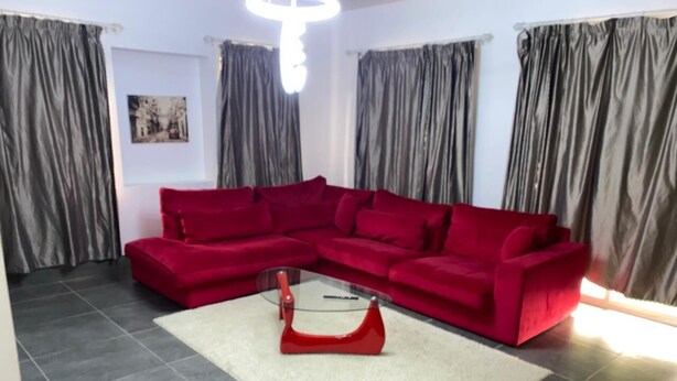 A living room with a red sectional sofa, a glass coffee table, and grey curtains. - Welcome to our app, "Unexpected" (onverwacht)