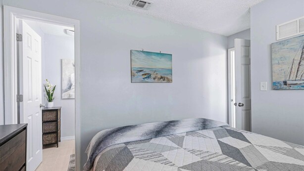 A bedroom with a bed, a door, a painting, and a small table with a plant. - Coastal Getaway on Okaloosa Island - 3 Minute Walk to Beach! (Fort Walton Beach)