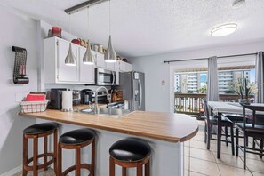 Eine moderne Küche mit einer zentralen Kochinsel, Barhocker, einem Essbereich mit Aussicht und einem Balkon.
