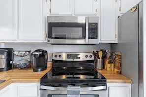 A kitchen with white cabinets, a stainless steel microwave, a Keurig coffee maker, a stove, and a knife block. - Coastal Getaway on Okaloosa Island - 3 Minute Walk to Beach! (Fort Walton Beach)