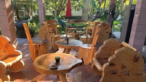 A wooden outdoor seating area with round tables and chairs, surrounded by a brick wall and greenery.