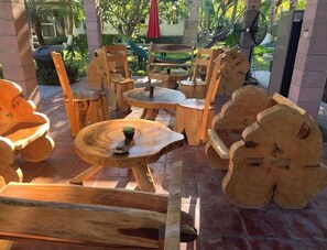 Een houten zitgedeelte buiten met ronde tafels en stoelen, omgeven door een bakstenen muur en groen.