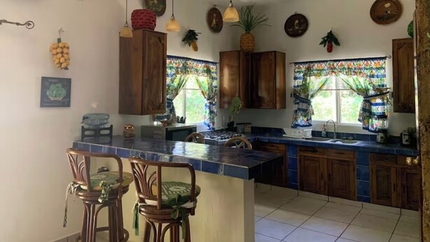 A kitchen with wooden cabinets, a central island, hanging pendant lights, and decorative wall art.