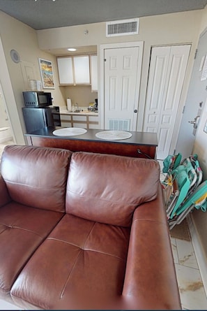 A brown leather sofa in a living area with a kitchen in the background. - Perfect Couples Retreat in North Myrtle (North Myrtle Beach)