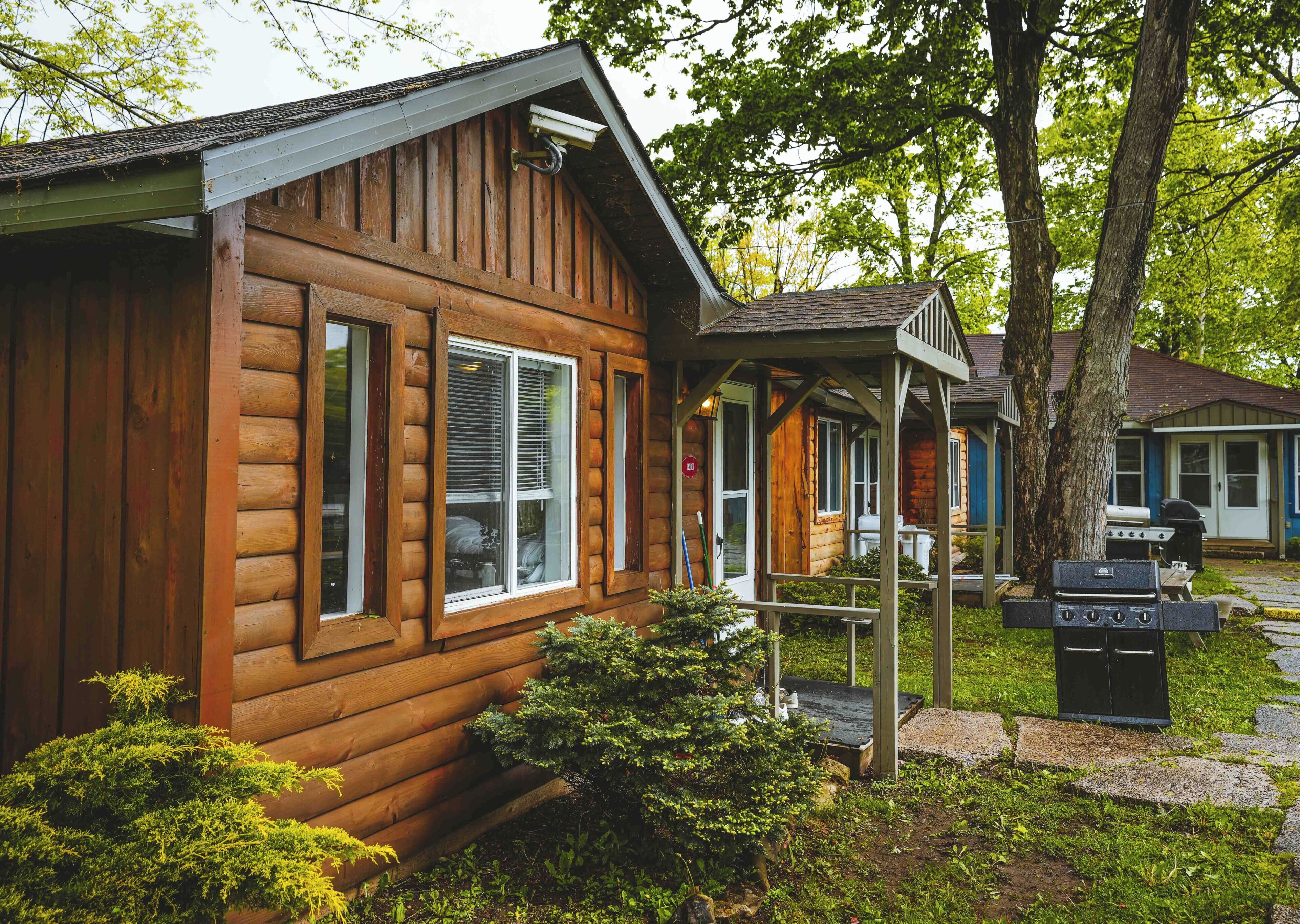 A wooden cabin with a porch, a grill, and a small garden area.