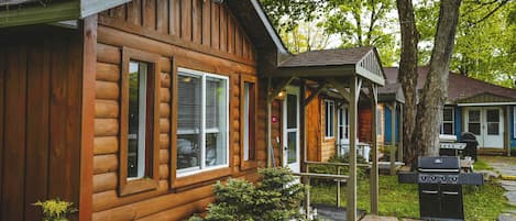 A wooden cabin with a porch, a grill, and a small garden area.