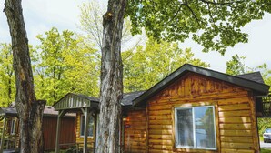 Eine Holzhütte mit Fenster und Veranda, umgeben von Bäumen und viel Grün.