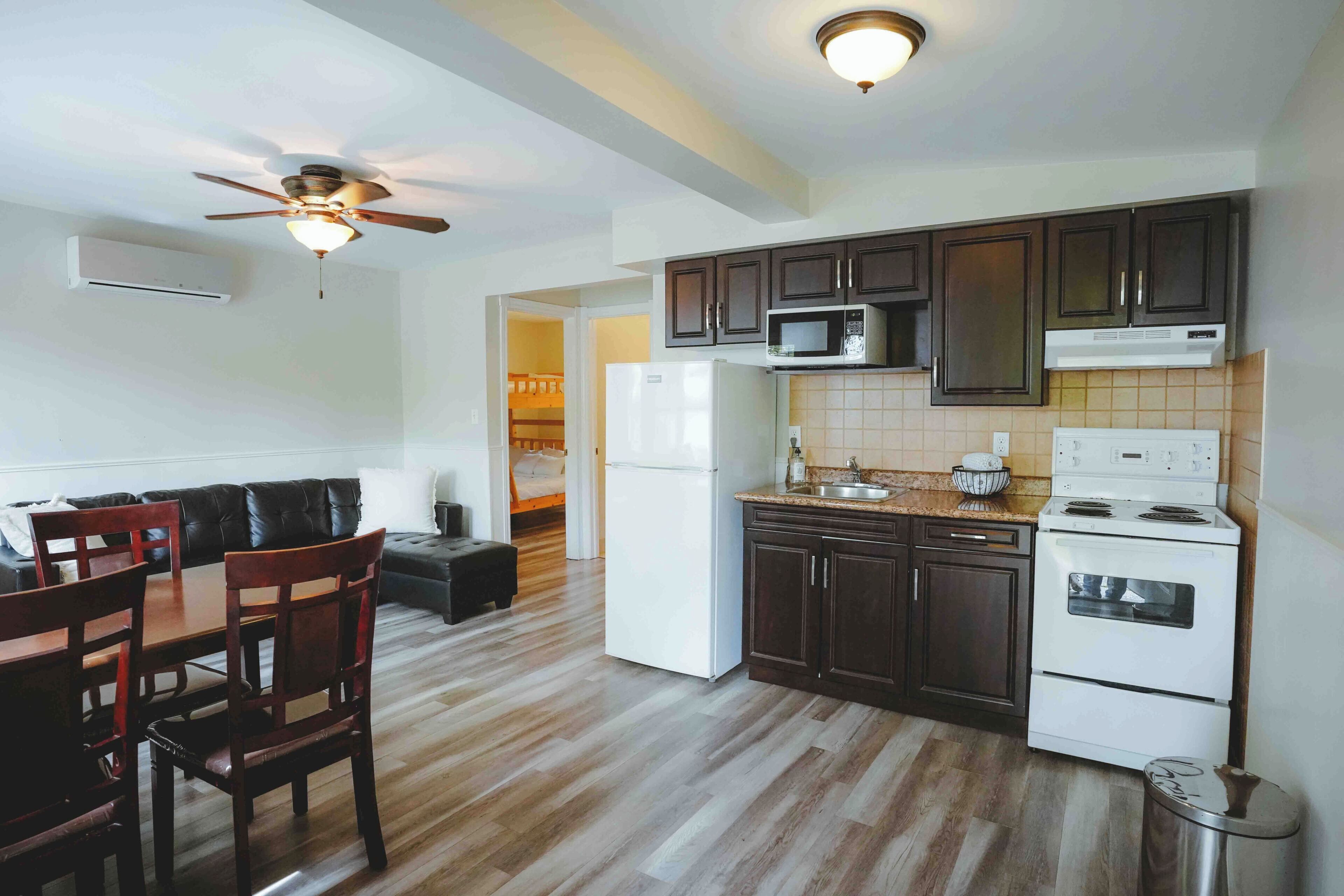 A modern kitchen with dark wood cabinets, a microwave, a refrigerator, and a stove. There is a dining area with a table and chairs.
