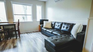 Ein Wohnzimmer mit Ecksofa, Esstisch und Stühlen sowie Holzdielen.