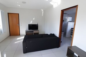 A modern living room with a black sofa, a flat-screen TV, and a wooden door. - DOURADOS GUEST FLAT PEDRA BONITA (Dourados)