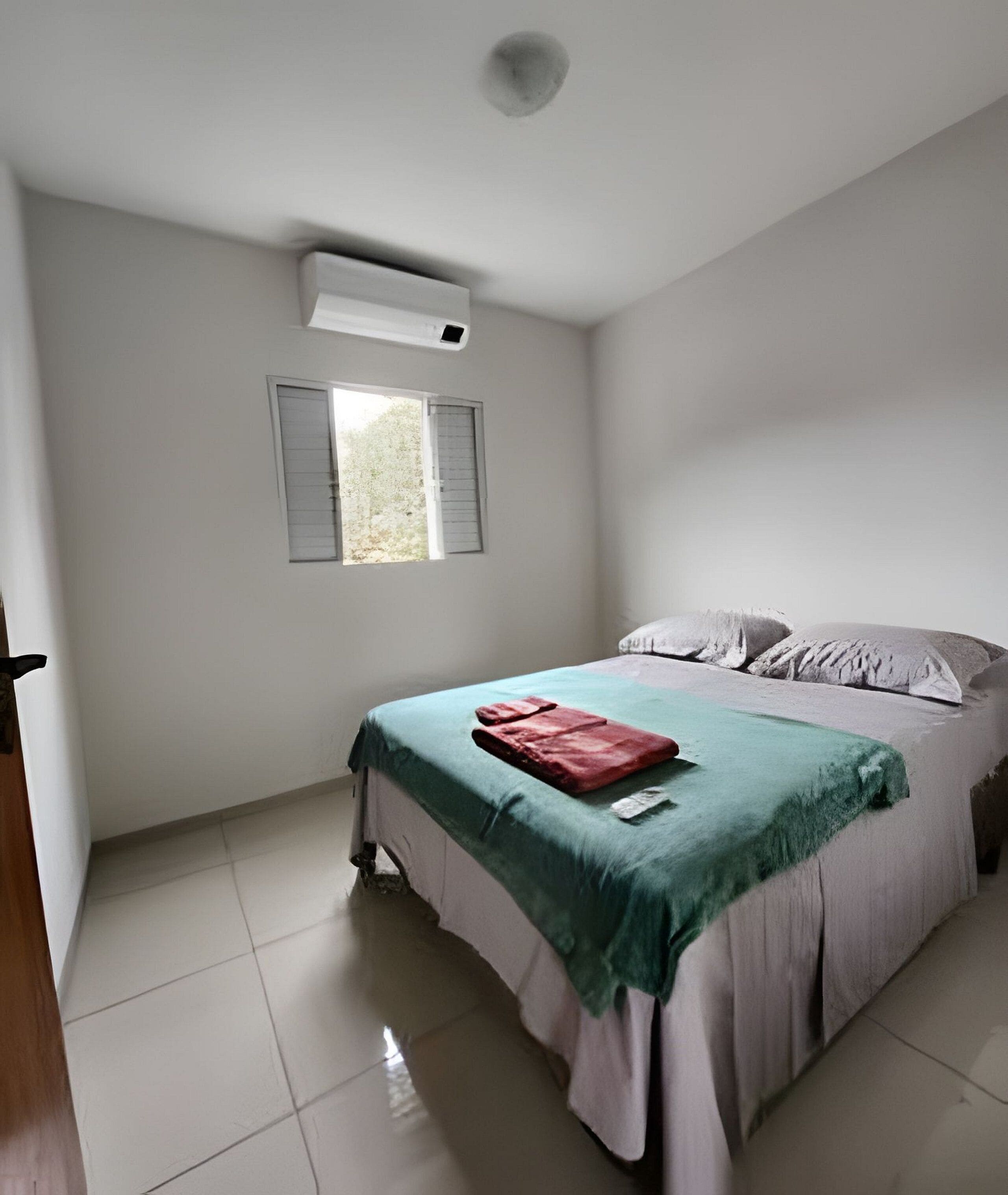 A bedroom with a bed, a window with shutters, and an air conditioning unit on the wall.