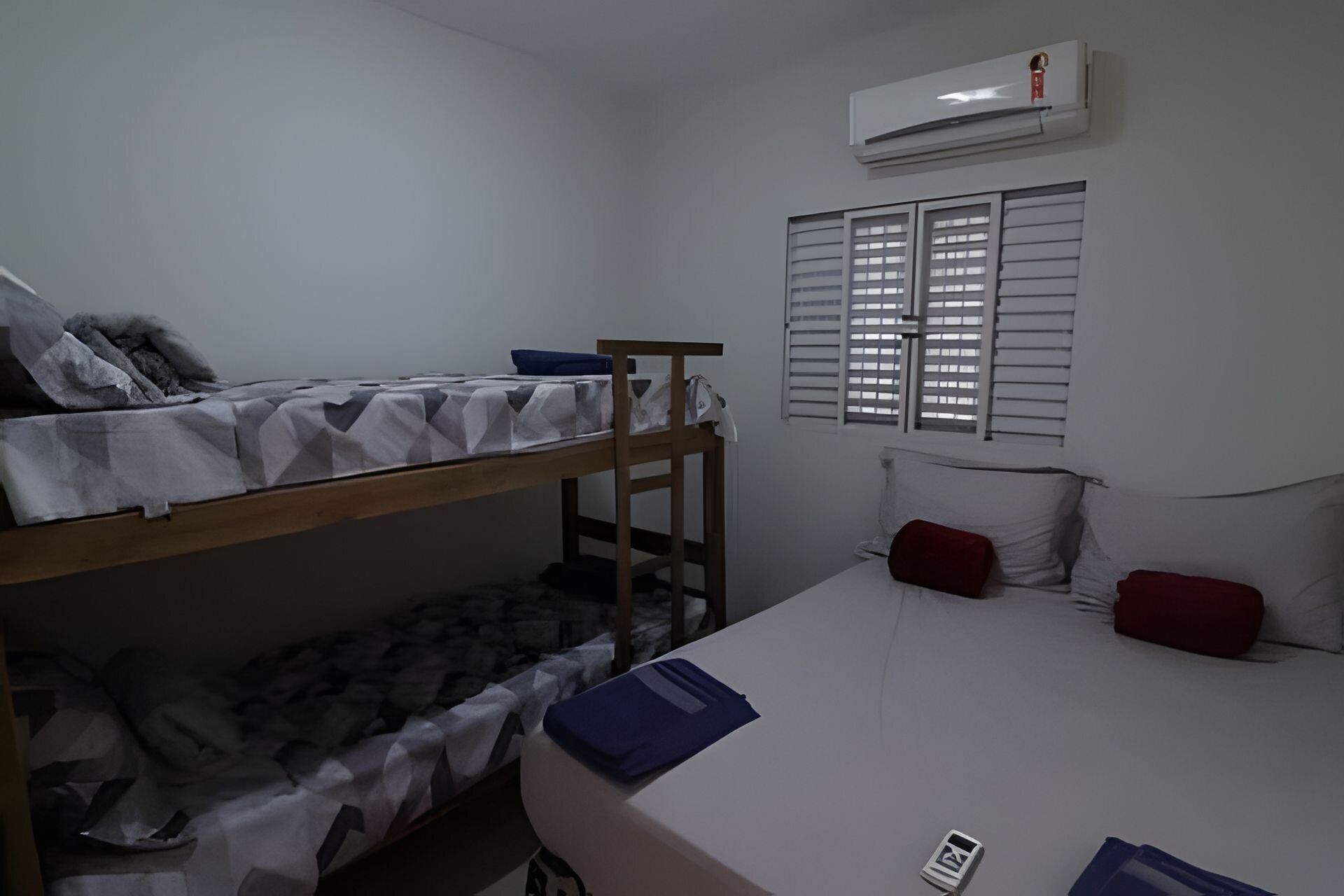 Un dormitorio con literas, un escritorio, una silla, una cama con almohadas, aire acondicionado y una ventana con persianas.