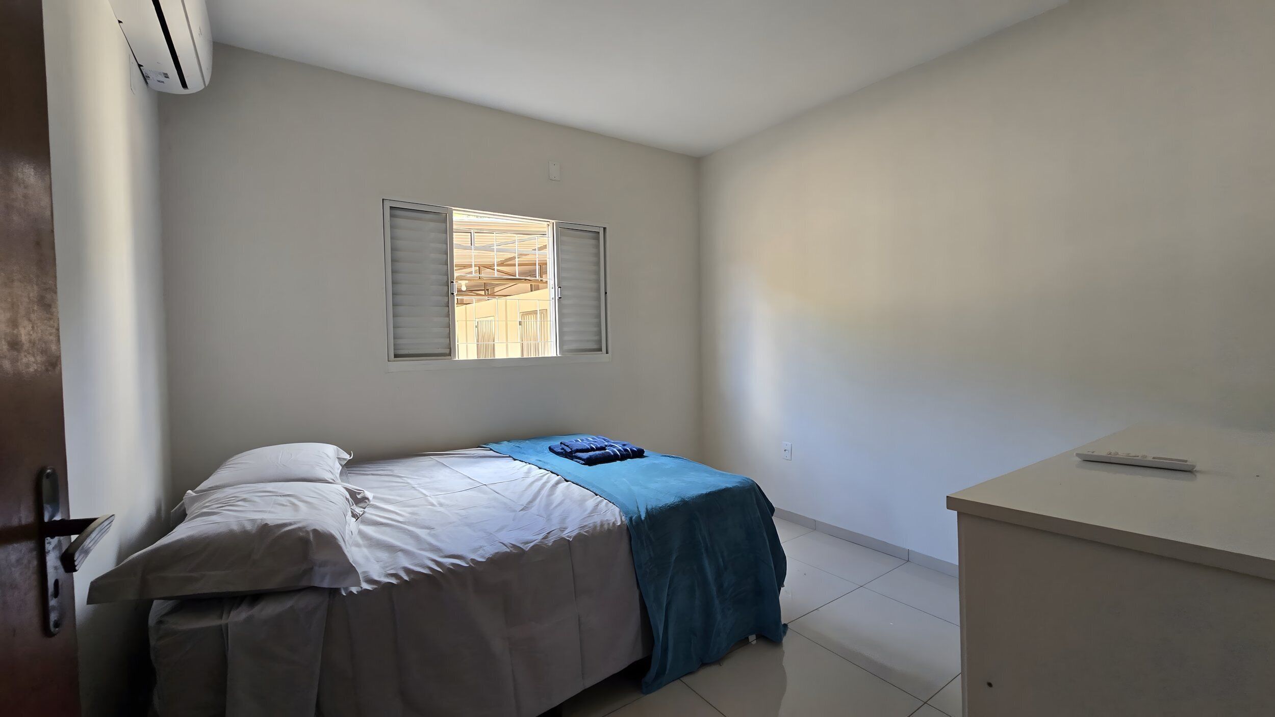 Una habitación pequeña y limpia con cama, escritorio y ventana con persianas.