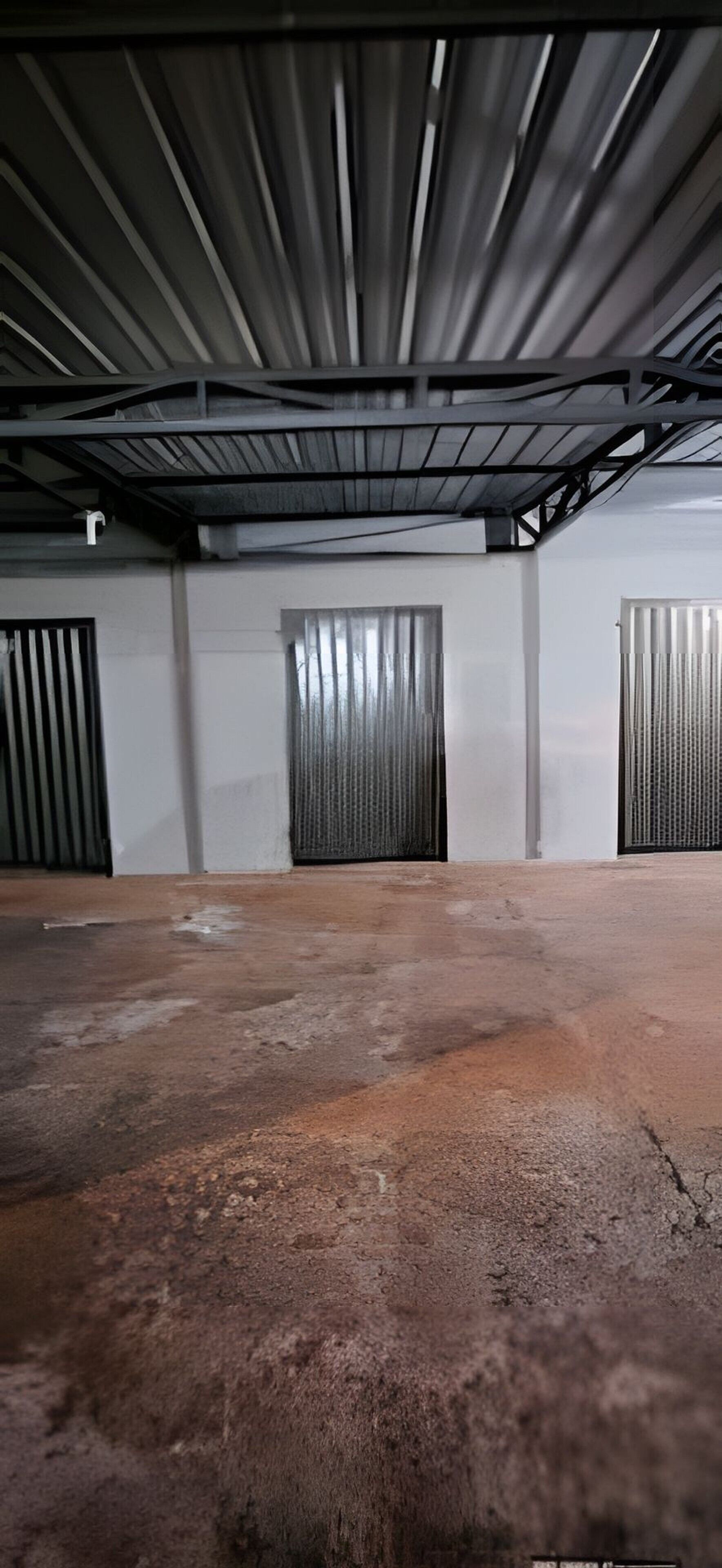 A warehouse interior with metal doors, a concrete floor, and a metal roof.