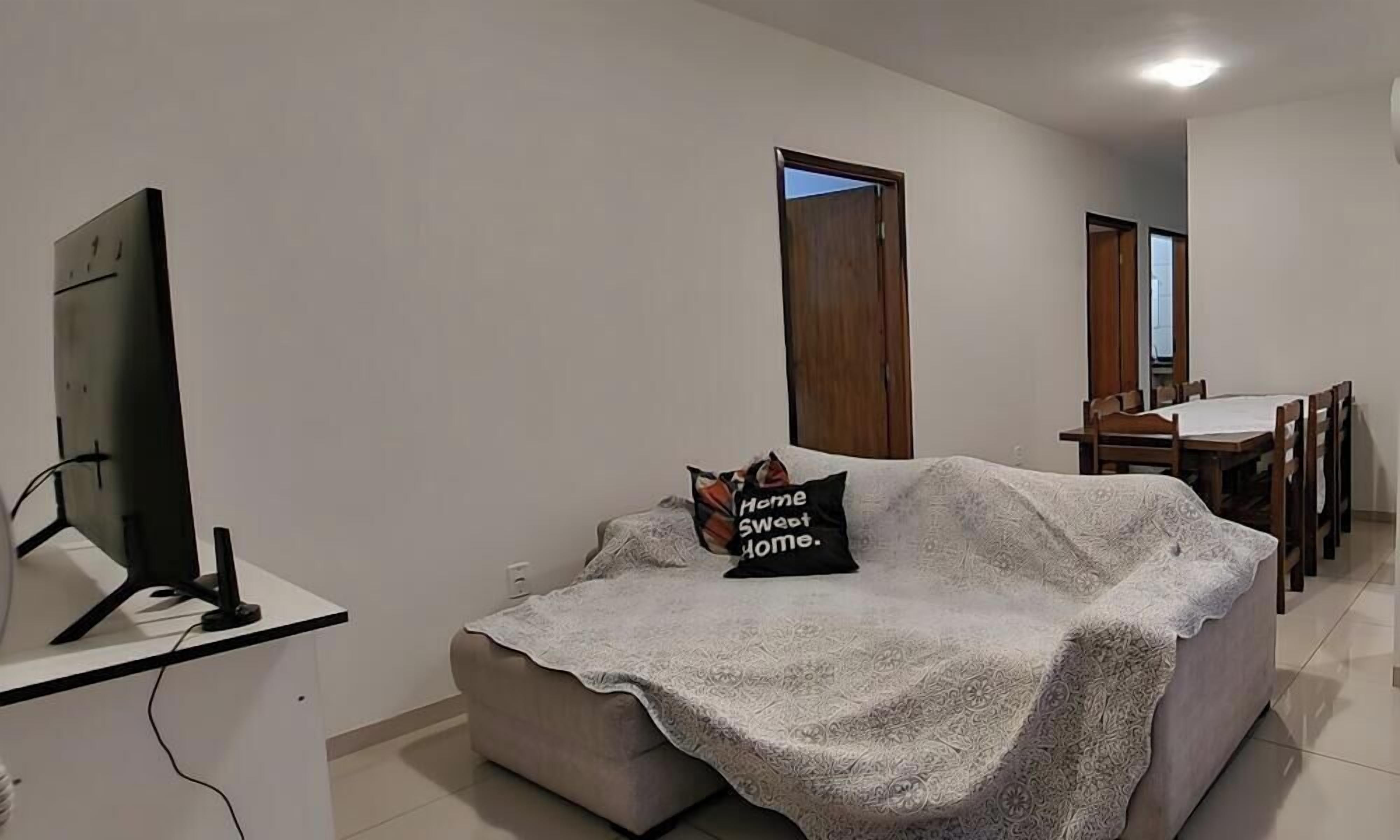 A living room with a sofa covered in a blanket, a television on a stand, and a dining area with a table and chairs.
