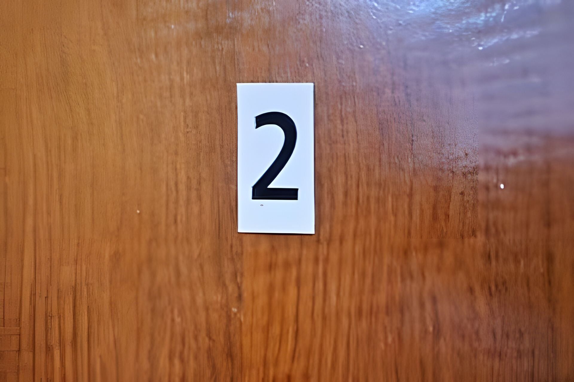Et hvidt skilt med tallet 2 på en træoverflade.