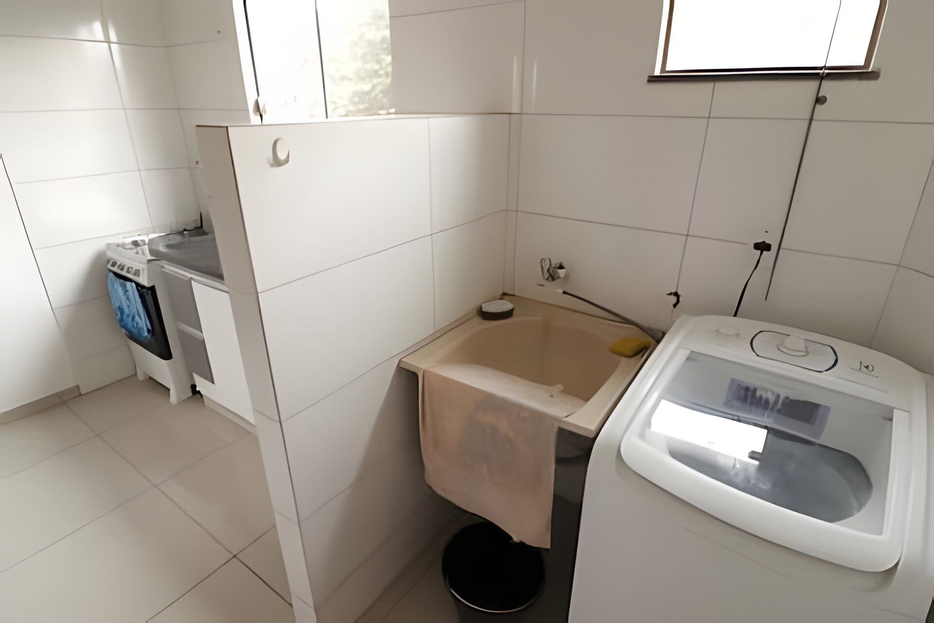 Um banheiro pequeno, revestido com azulejos, com uma máquina de lavar branca, uma banheira e uma janela.