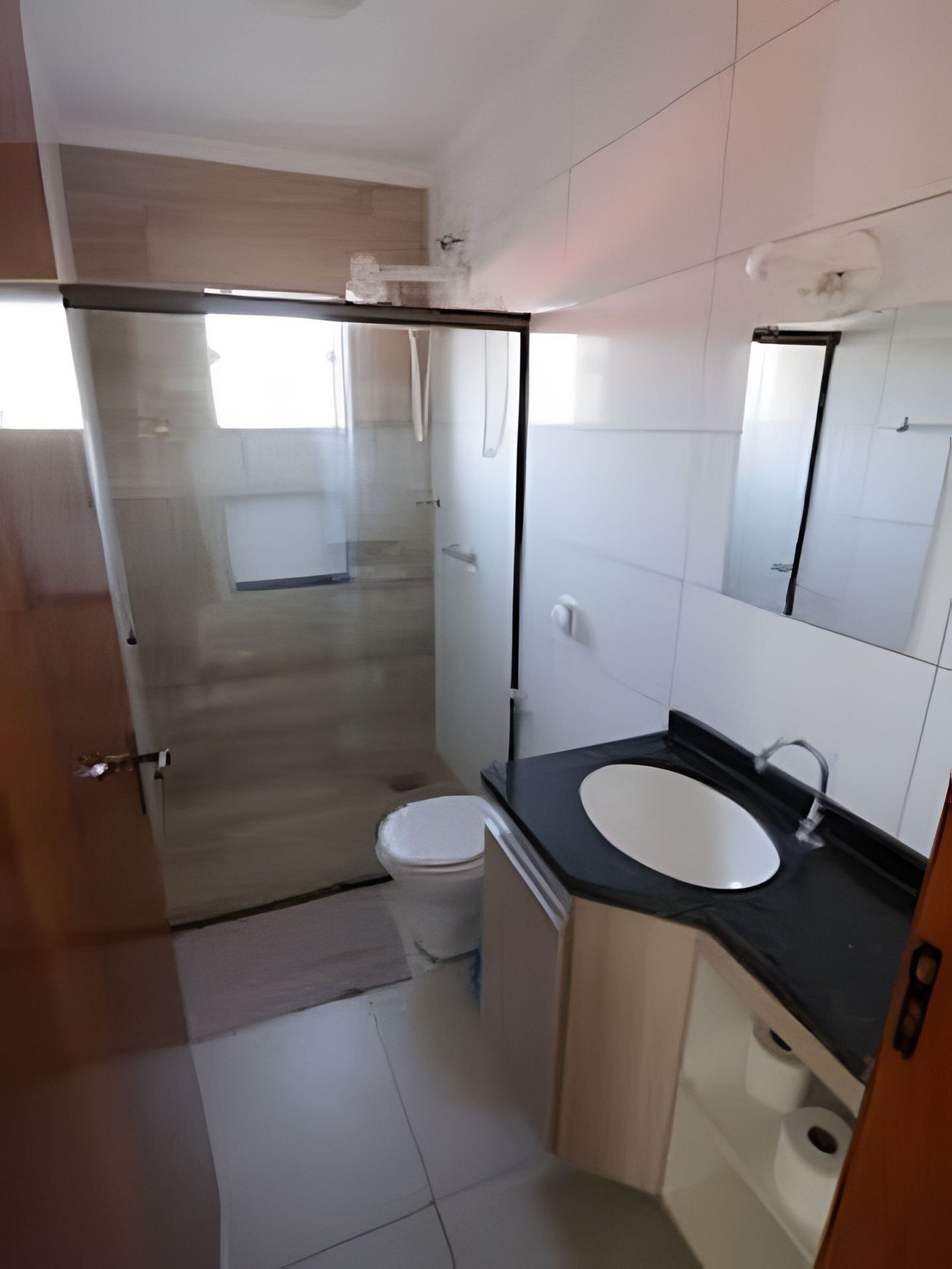 Uma casa de banho moderna com chuveiro em cabine de vidro, sanita branca e lavatório com bancada preta.