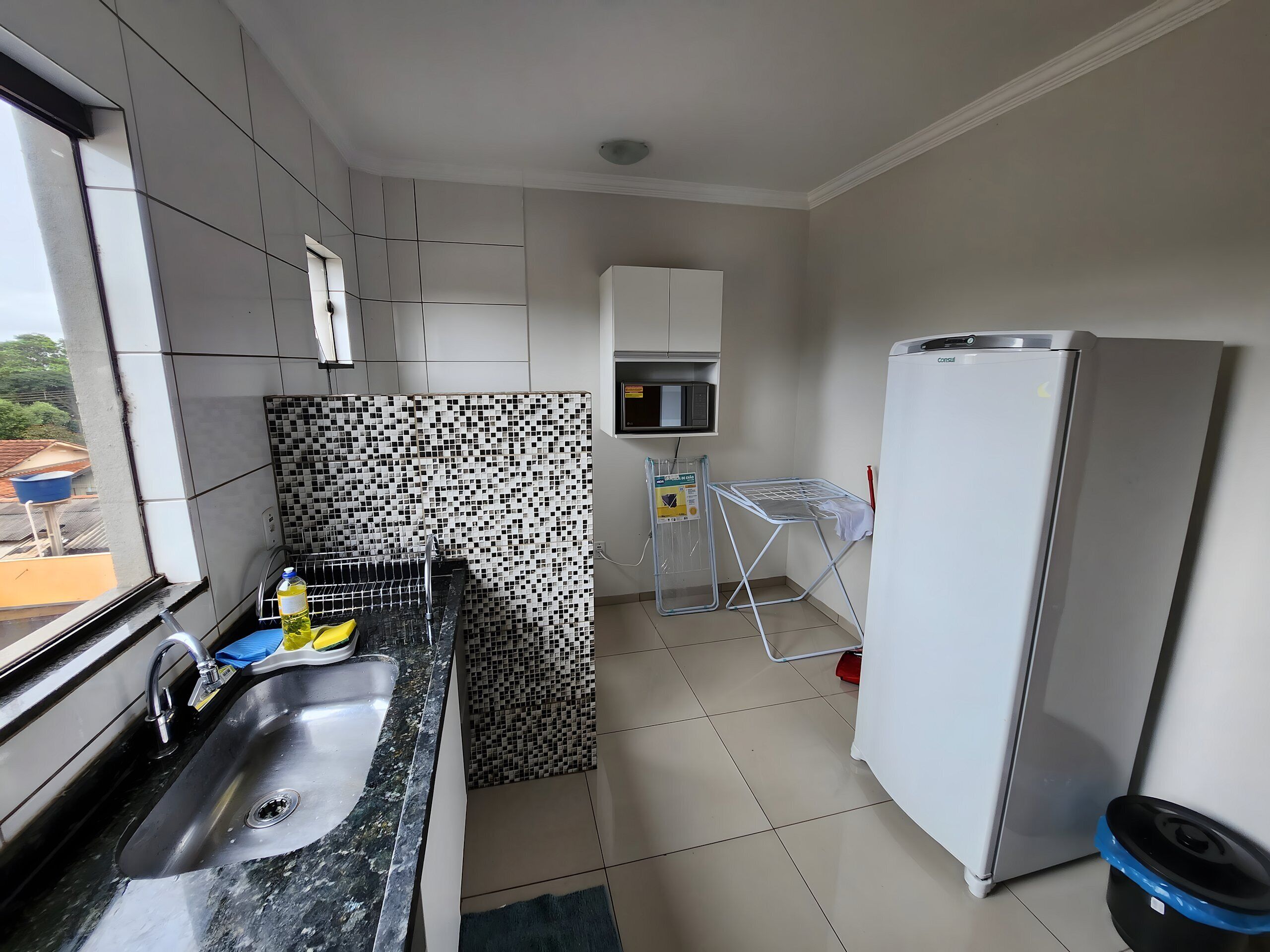 Uma cozinha moderna com pia de aço inoxidável, micro-ondas, geladeira e painel de fundo com padrão.