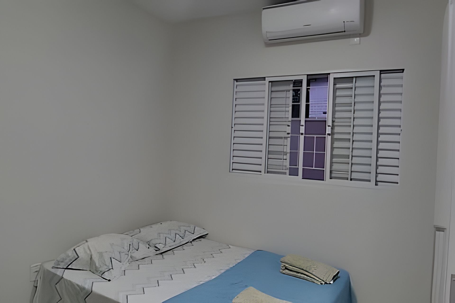 Una habitación con cama, aire acondicionado y ventana con contraventanas.