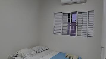 Una habitación con cama, aire acondicionado y ventana con contraventanas.