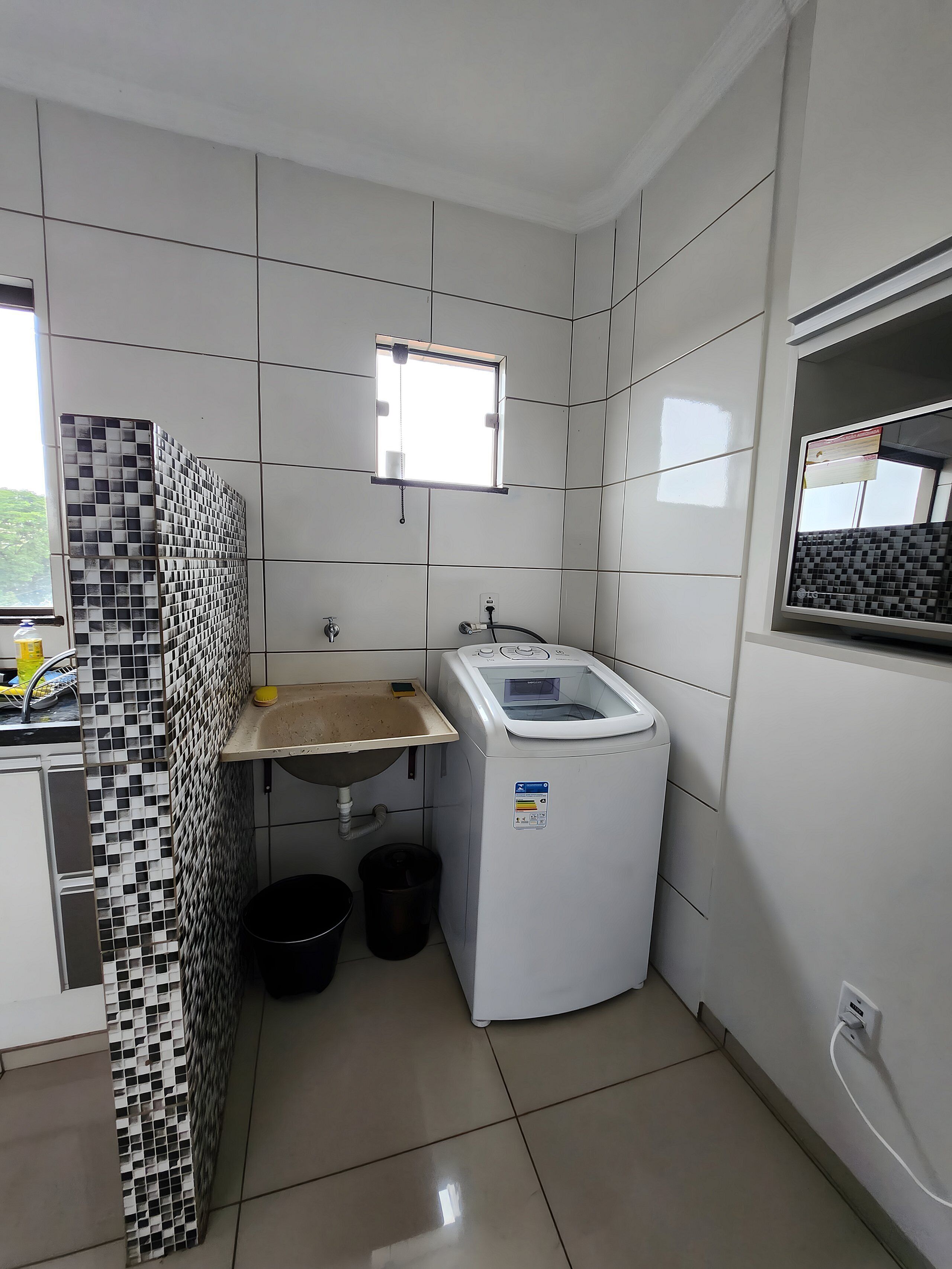 A small, clean laundry room with a washing machine, a sink, and a window.