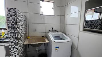 A small, clean laundry room with a washing machine, a sink, and a window.