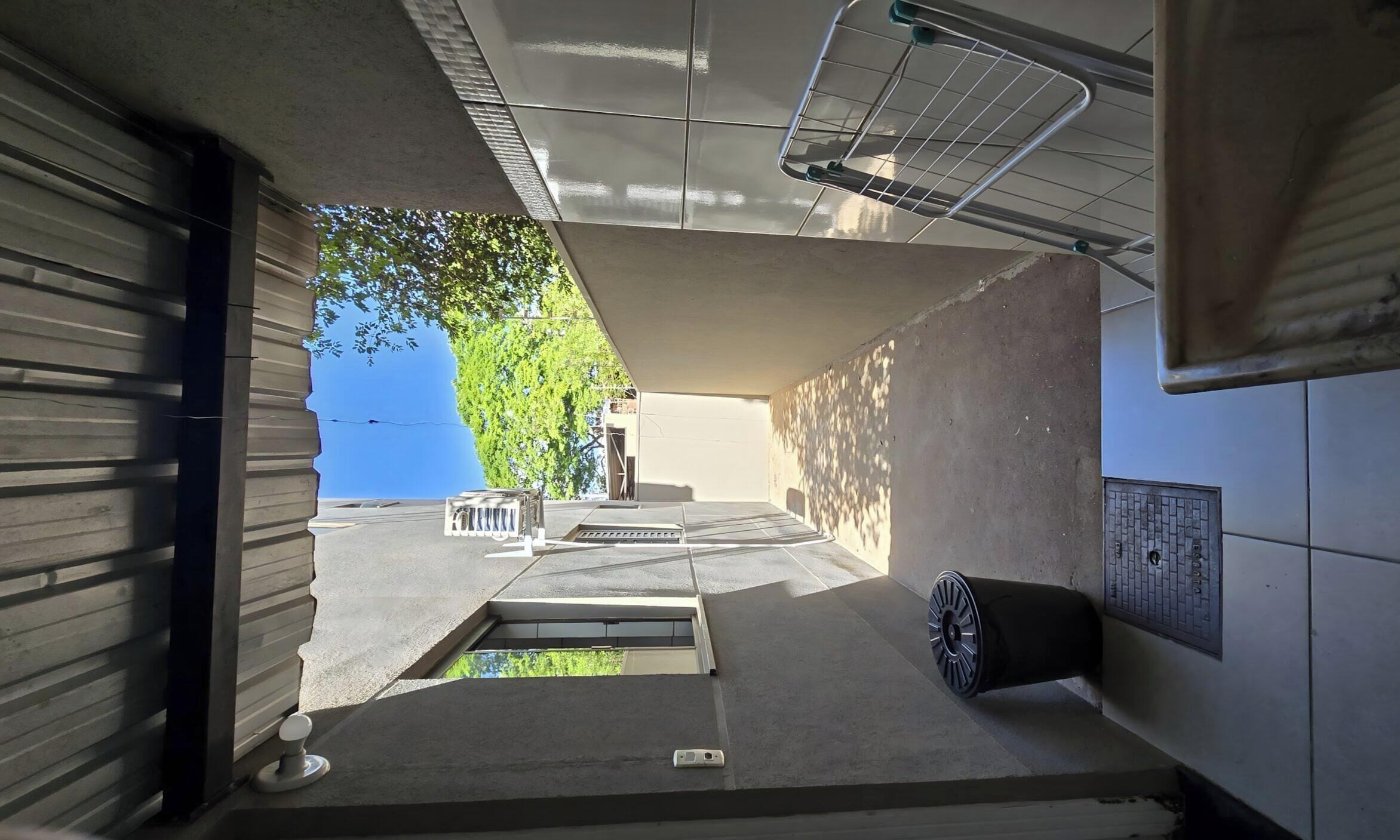 A narrow corridor with a concrete floor, a metal vent, and a tiled wall.