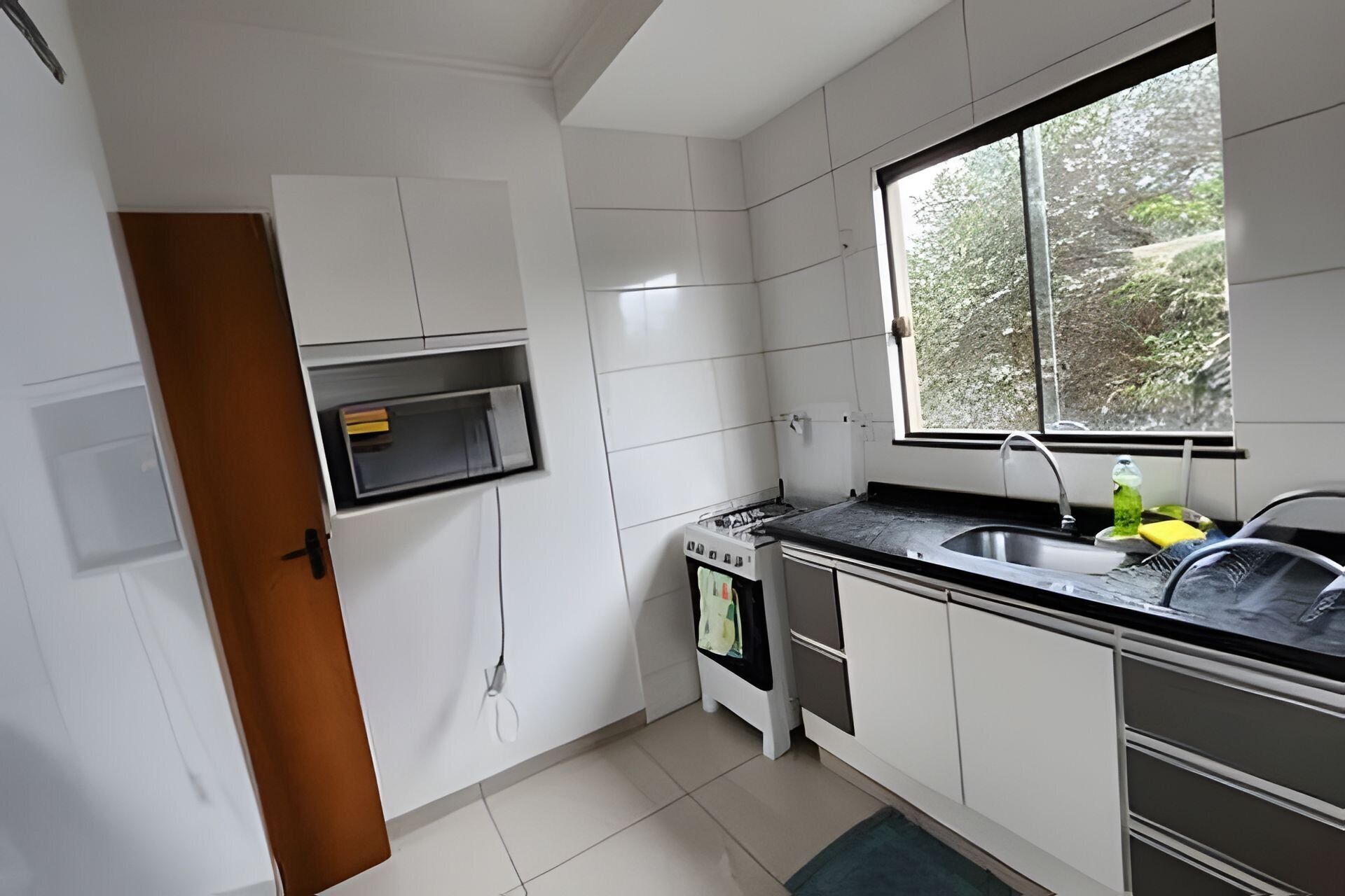 Una cocina con armarios blancos, microondas integrado, estufa y ventana con vista a árboles.
