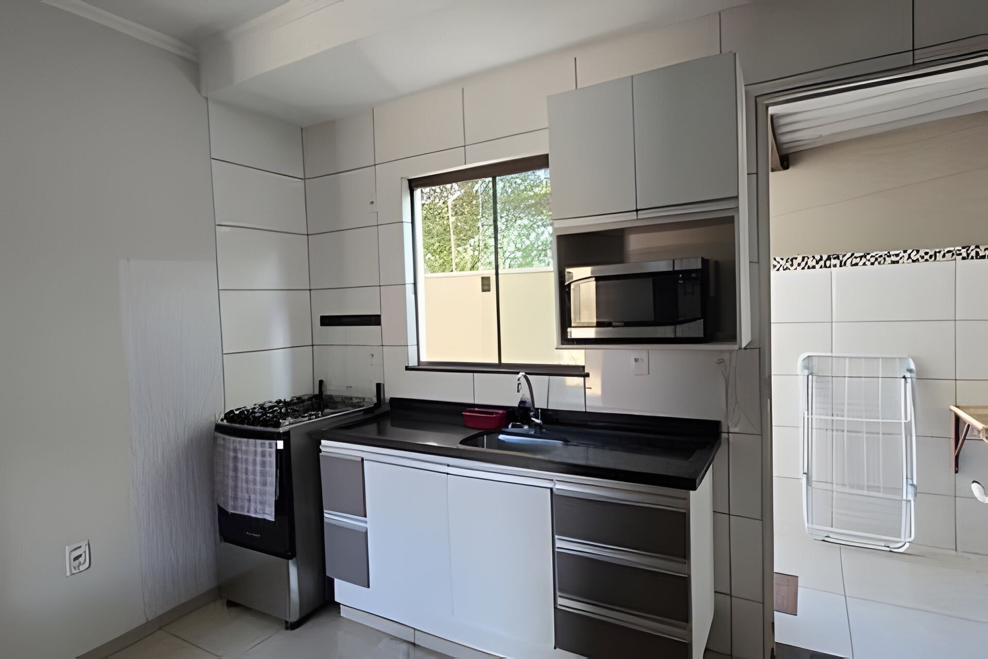 A modern kitchen with white cabinetry, a stainless steel refrigerator, a microwave, and a window providing natural light.