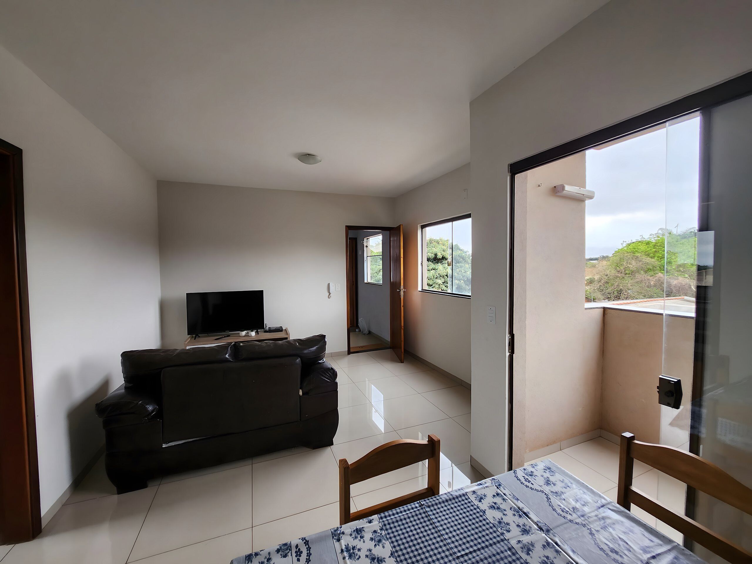 Una sala moderna con un televisor de pantalla plana, un sofá de color oscuro y una mesa de comedor con sillas.