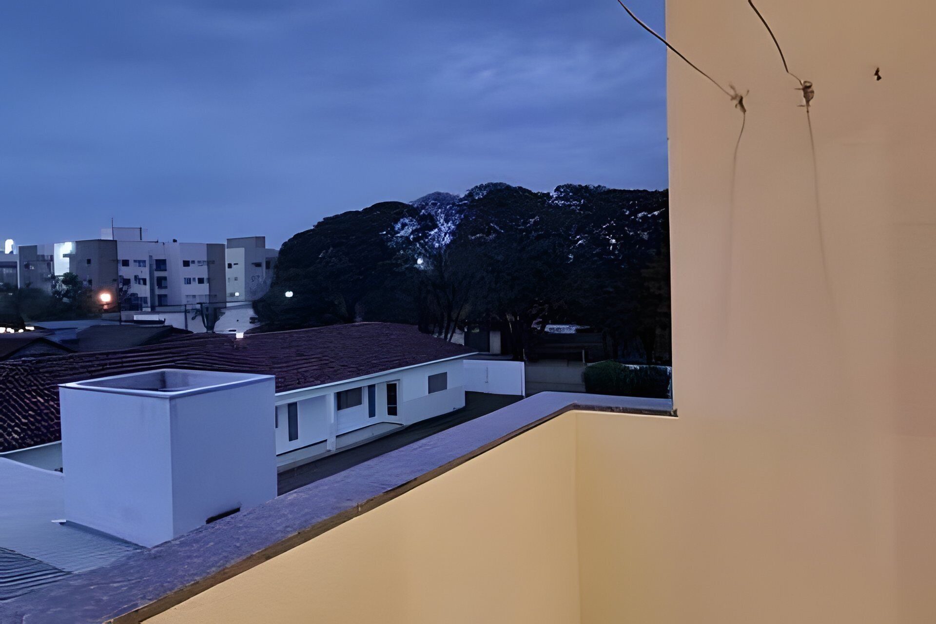 Um bairro residencial com um edifício de telhado plano, uma parede externa branca e uma rua arborizada ao entardecer.