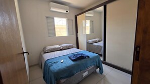 Un dormitorio con cama, ventana, equipo de aire acondicionado y puerta corredera.