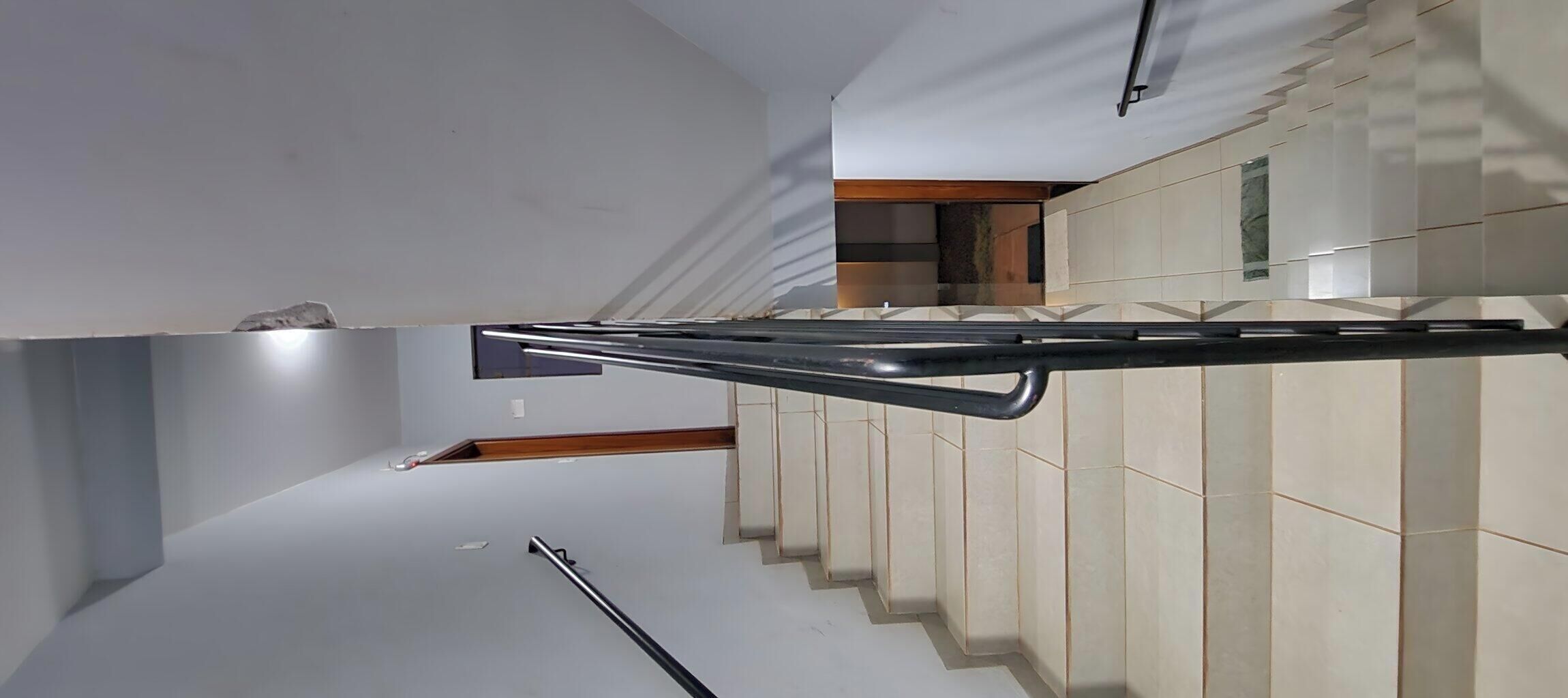 A staircase with a handrail, leading to a room with a wooden floor and a tiled wall.