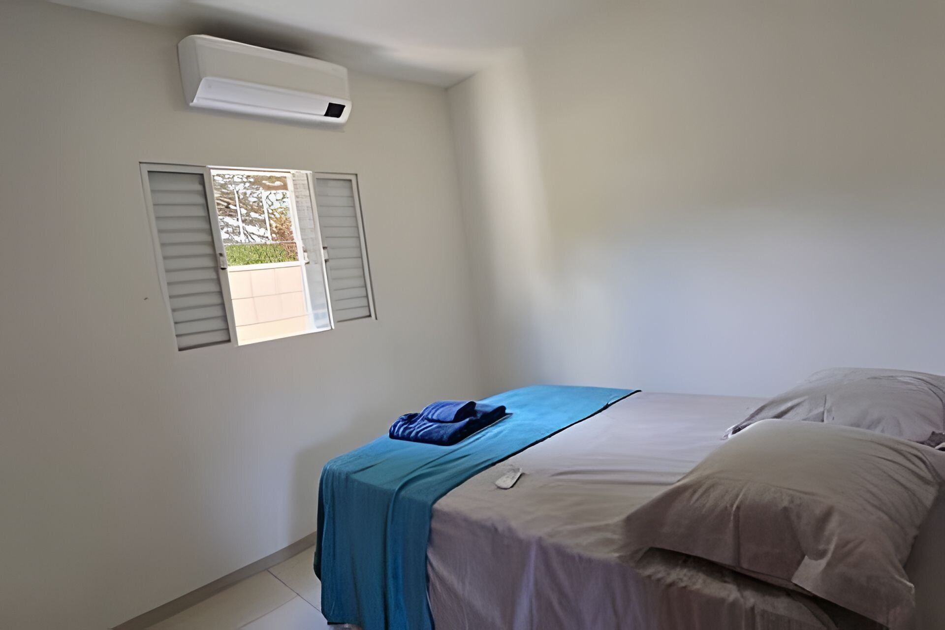 Un dormitorio con cama, ventana con persianas y un equipo de aire acondicionado.