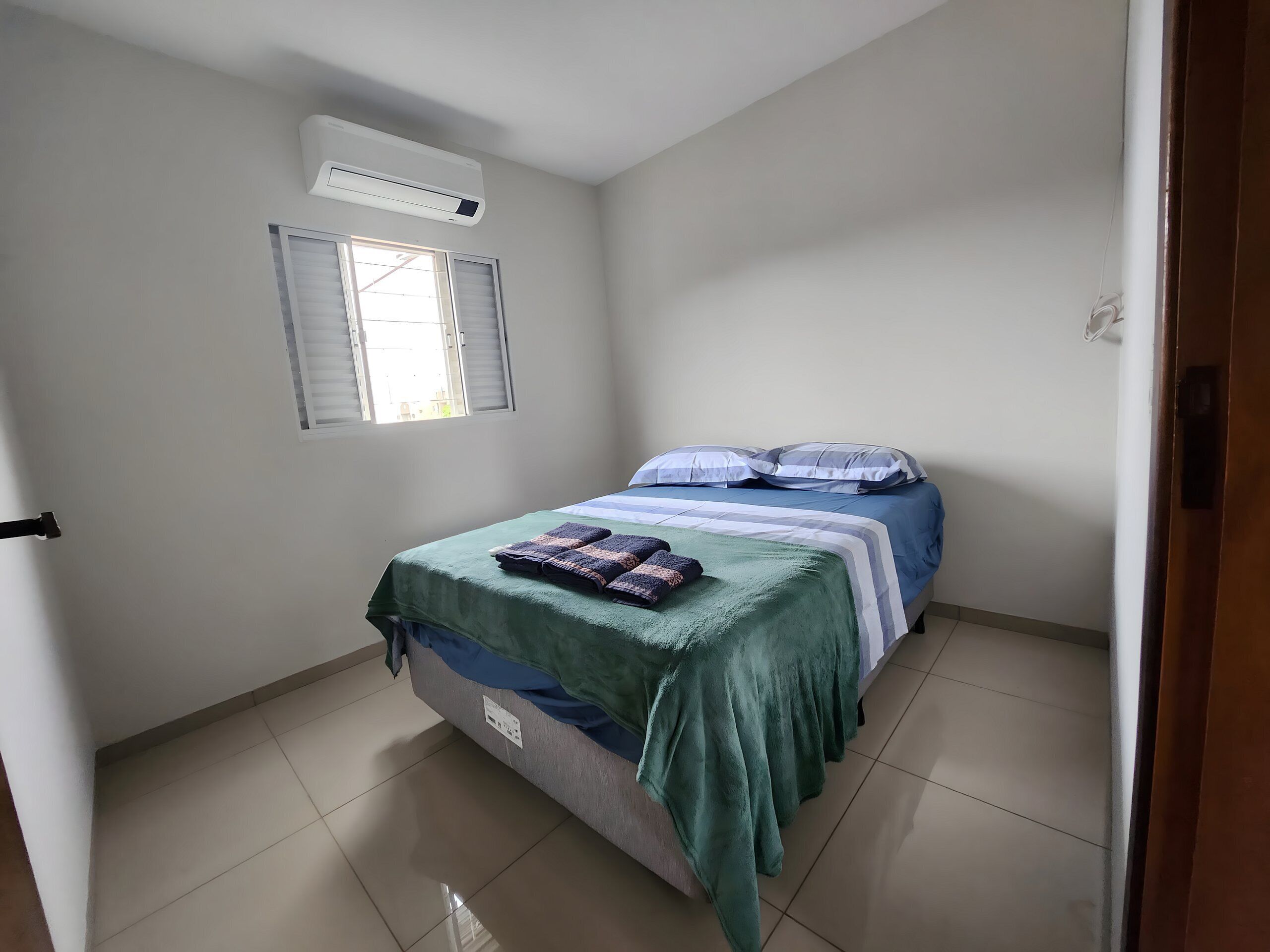 A bedroom with a bed, a window, and an air conditioning unit.