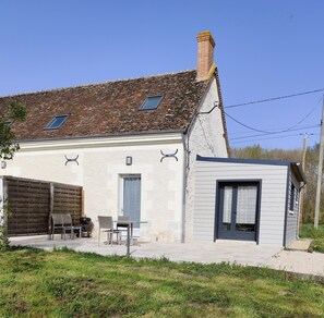 A two-story house with a stone roof, a small attached garage, and a patio with outdoor seating. - Holiday Home 'Maison campagne proche Beauval 2p' with Terrace, Private Garden & Wi-Fi (Selles-sur-Cher)
