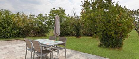 An outdoor patio with a table and chairs, surrounded by a well-maintained lawn and hedges.