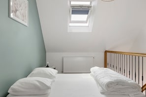 A bedroom with a sloped ceiling, a skylight, a radiator, a bed with white bedding, and a wooden headboard.
