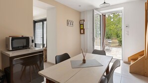 A modern kitchen with a microwave, a dining table with chairs, and a view of the outdoors through a glass door.