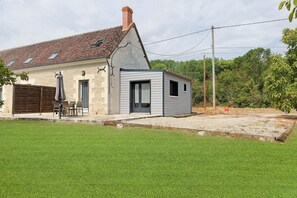 A two-story house with a tiled roof, a fenced patio with outdoor furniture, and a gravel driveway.
