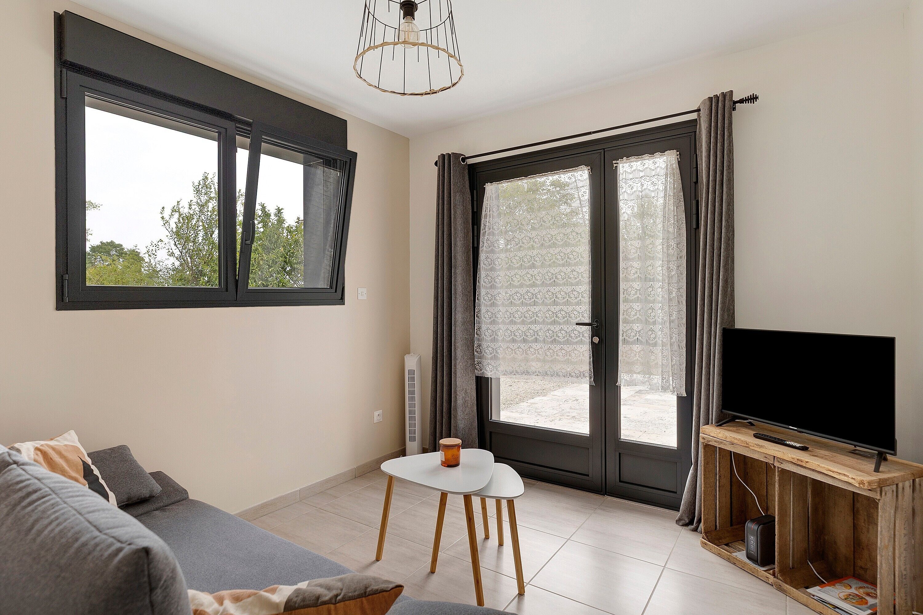 Un salon moderne avec un canapé, une petite table, un téléviseur et une grande fenêtre avec des rideaux.