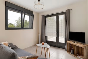 Una sala de estar moderna con un sofá, una mesita, un televisor y un ventanal con cortinas.
