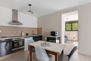 A modern kitchen with a dining area, a built-in oven, a microwave, and a window providing a view of greenery. - Holiday Home 'Maison campagne proche Beauval 2p' with Terrace, Private Garden & Wi-Fi (Selles-sur-Cher)