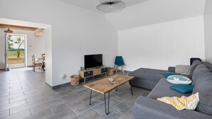 A modern living room with a grey sofa, a wooden coffee table, a TV on a wooden stand, and a hanging light fixture.