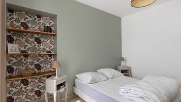 A bedroom with a bed, a nightstand, a lamp, and a shelf with a floral wallpaper.