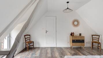Une pièce avec un plafond en pente, une porte blanche, deux chaises en bois, une commode en bois, un luminaire suspendu et un objet décoratif fixé au mur.