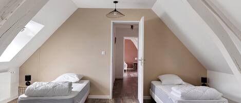 Una habitación con dos camas, techo inclinado y una puerta que da a otra habitación.